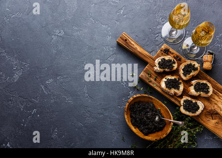 Schwarz von Störkaviar in Holzschale, Sandwiches und Champagner auf dunklem Stein Textfreiraum Stockfoto