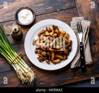 Gebratene Kartoffeln gebraten mit Steinpilzen wild auf weißen Teller und Frühlingszwiebeln auf Holztisch Hintergrund Stockfoto