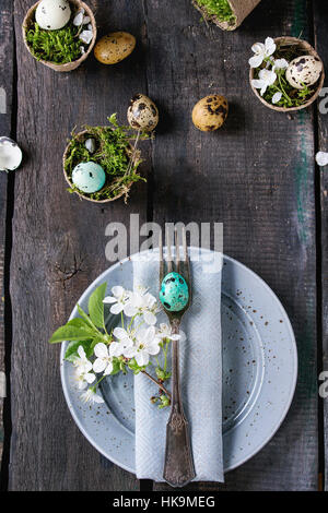 Tabelle Einstellung Dekor bunte Ostern Wachteleier mit Kirsche Frühlingsblumen, Moos im Garten Töpfe leeren Tellern, Besteck über alte Holz Hintergrund. Dunklen r Stockfoto