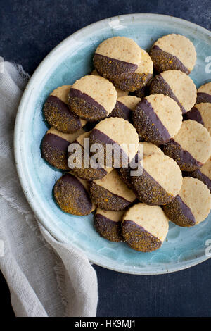 Shortbread-Plätzchen in Schokolade getaucht und Kurkuma Zucker mit Milch serviert. Aus der Draufsicht auf schwarz/grau Hintergrund fotografiert. Stockfoto