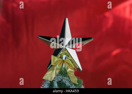 Spitze der Weihnachtsbaum mit Stern in hellen roten glänzenden Hintergrund dekoriert. Stockfoto