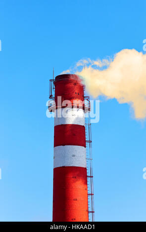 Rote und weiße Fabrikschlot mit Rauch gegen blauen Himmel Stockfoto