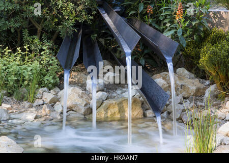 Moderner, moderner Garten mit einem kleinen Teich und Rillwasser aus recyceltem Wasserfall über Steinfelsen und Felsbrocken in Großbritannien Stockfoto