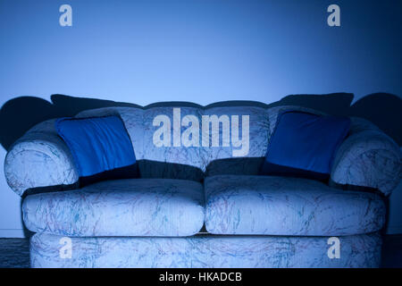 Mann in Hemd und Jeans sitzt auf dem Sofa vor dem Fernseher in der Dunkelheit mit Fernbedienung Stockfoto