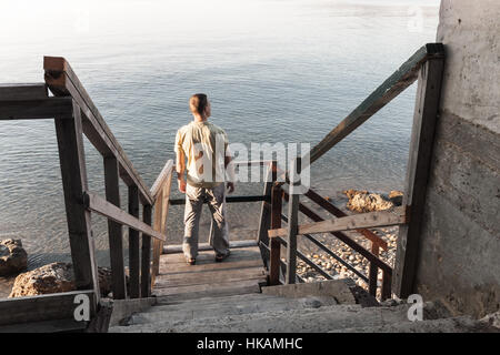 Junger Mann steht auf alte Holztreppe hinunter zur Küste Meeres Stockfoto