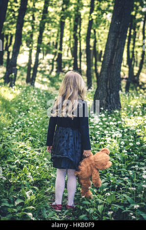 verlorene Mädchen im schwarzen Kleid mit Teddybär Spielzeug im Frühjahr Wald wieder anzeigen Stockfoto