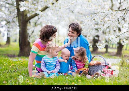 Große Familie mit drei kleinen Kindern beim Mittagessen im Freien. Eltern und Kinder mit Picknick-Korb im Frühlingsgarten. Stockfoto