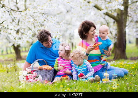 Große Familie mit drei kleinen Kindern beim Mittagessen im Freien. Eltern und Kinder mit Picknick-Korb im Frühlingsgarten. Stockfoto