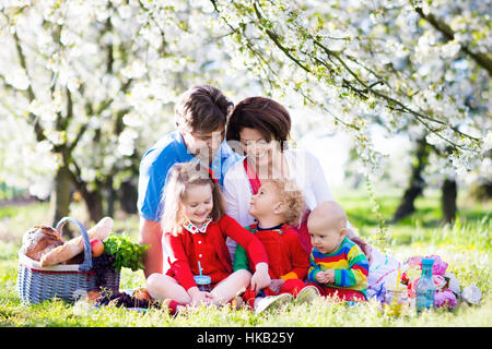 Große Familie mit drei kleinen Kindern beim Mittagessen im Freien. Eltern und Kinder mit Picknick-Korb im Frühlingsgarten. Stockfoto