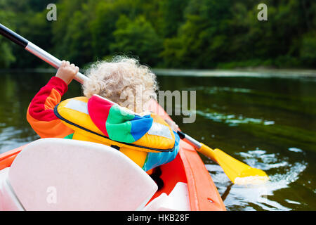 Glückliches Kind genießen Kajakfahrt auf schönen Fluss. Kleinen lockigen Kleinkind Jungen Kajak an heißen Sommertag. Wassersport und camping Stockfoto