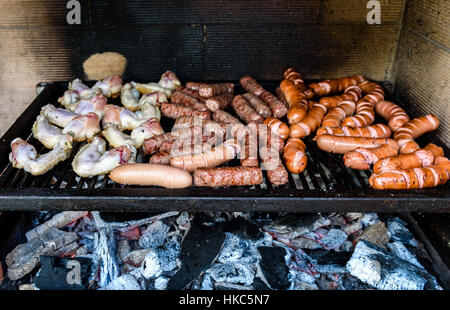 Gemischte Auswahl an Fleisch auf Grill mit Kohle. Cevapcici, Würstchen, Chicken Wings und Hot Dogs auf Holzkohle Grill BBQ. Stockfoto