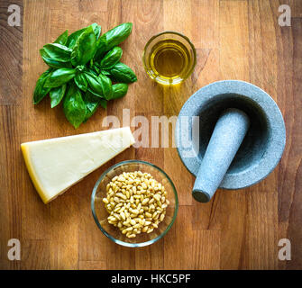 Herstellung von selbstgemachtem Pesto Genovese mit allen Zutaten. Basilikum, Olivenöl, Parmesan-Käse und Mühle auf einem Schreibtisch aus Holz. Everythe Zutat für die Herstellung Stockfoto