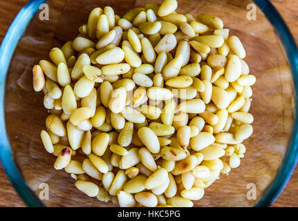 Pinienkerne oder Samen in Glasschüssel auf hölzernen Hintergrund. Nahaufnahme von Pinienkernen servieren oder zum Kochen bereit. Stockfoto