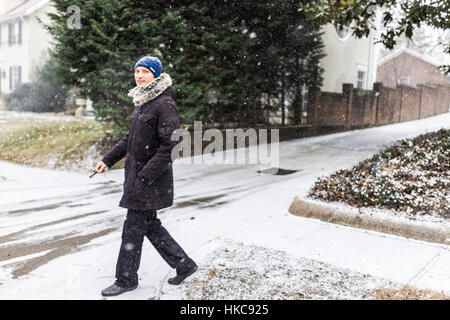 Junger Mann mit Autoschlüssel zu Fuß auf Bürgersteig in Mantel im Winterschnee Stockfoto