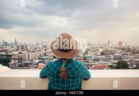 Tourist-Frau in Hut und grün kariertes Hemd Blick auf Bangkok City Panorama mit Wolkenkratzern des Geschäftsviertels von Golden Mountain Wat Saket roo Stockfoto