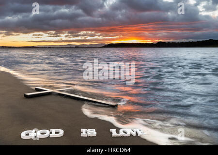 Kreuz am Flussstrand mit den Worten "Gott ist Liebe" darunter. Stockfoto