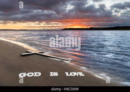 Kreuz am Flussstrand mit den Worten "Gott ist Liebe" darunter. Stockfoto