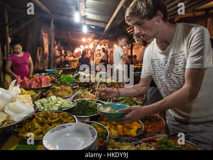 LUANG PRABANG, LAOS - 15. Mai 2015: Ein junger kaukasischer Tourist kauft Lebensmittel von einem Marktstand in Luang Prabang Nachtmarkt. Stockfoto