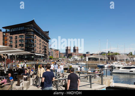 OSLO - 16. Mai 2016: Menschen genießen Sie Mittagessen in den Restaurants entlang der renovierten Aker Brygge Hafen an einem sonnigen Tag in Norwegens Hauptstadt. Das Gebäude in t Stockfoto