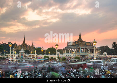 PHNOM PENH, Kambodscha - 24. Januar 2016: Vor dem königlichen Palast bei Sonnenuntergang in Kambodschas Hauptstadt Autos und Motorräder eilen. Stockfoto