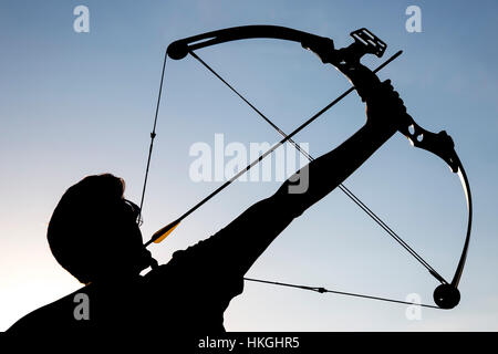 Eine Silhouette eines Bogenschützen zieht seine Verbundbogen und strebt nach oben mit klaren blauen Himmel als Hintergrund. Stockfoto