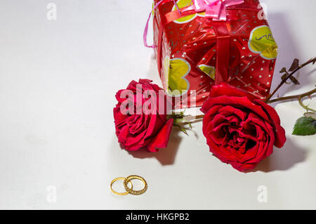Helle rote Rosen mit Gold Verlobungsringe und wickelte Geschenk los in Weiß isoliert. weißer Raum für romantische Inhalt der Nachricht. Stockfoto