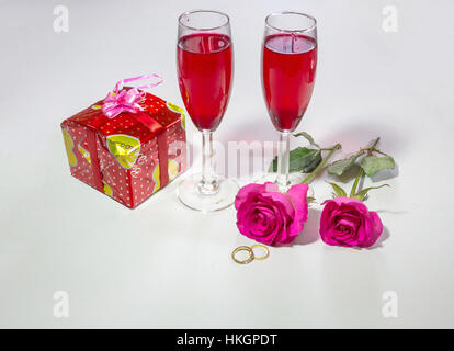 Romantische Valentines Tag Setup mit leuchtend rosa Rosen verpackte Geschenk Stein Verlobungsringe und Gläser Rotwein. Stockfoto