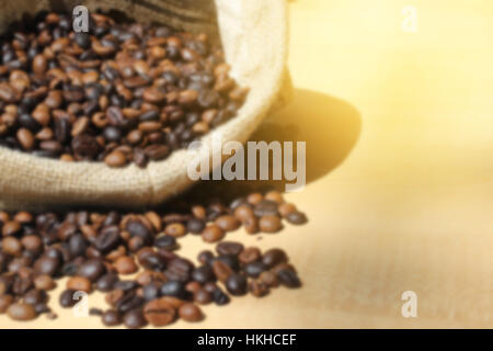 unscharfen Foto, gerösteten Kaffeebohnen in Sackbeutel auf Holztisch Stockfoto