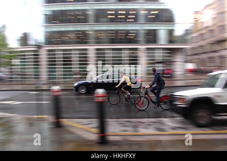 Schwenken Schuss 2 Radfahrer und Autos in einer Londoner Straße an einem regnerischen Tag. Stockfoto