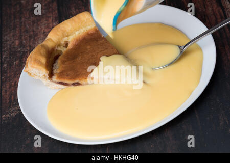 Eine Scheibe von Bakewell Pudding mit Vanillesauce. Stockfoto