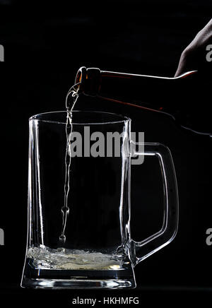 Gießen Bier in leere Glas Flasche auf schwarzem Hintergrund Stockfoto