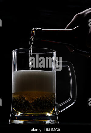 Gießen frisches Bier aus der Flasche auf schwarz Stockfoto