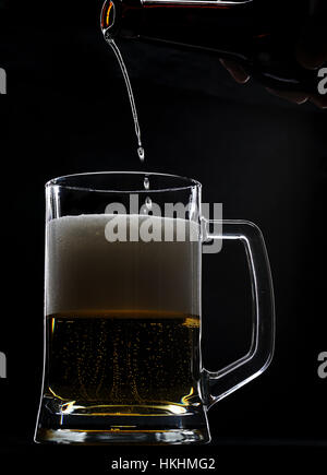 Letzte Tropfen Bier gehen in Glas von Flasche auf schwarz Stockfoto