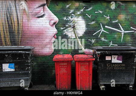 Graffiti in Glasgows Hinterstraße, blonde Frau bläst einen Löwenzahn in Windturbinen, erzeugt grüne Energie, in der Nähe von Mülltonnen Stockfoto