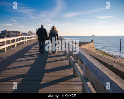 Ein paar gehen hand in hand entlang Southsea Seafront in Portsmouth, Hampshire, England an einem klaren Wintertag Stockfoto