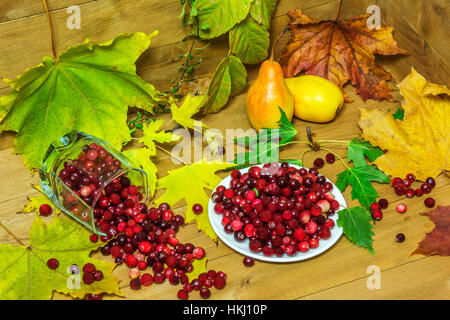 Auf eine Holzfläche umgeben von Herbst Blätter liegen Birnen und Preiselbeeren in einem weißen Teller und gefallenen Becherglas Stockfoto