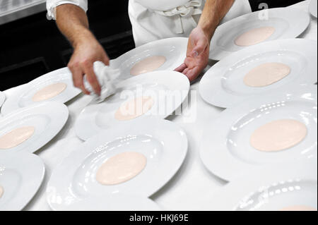 Ernte-Blick auf inkognito Kellner in weißer Schürze Holding Serviette beim Abwischen weißer Platten mit rosa Zentrum über Tisch im restaurant Stockfoto