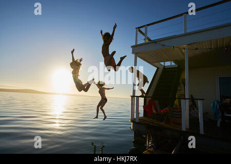 Junge Erwachsene Freunde abspringen Sommer Hausboot in Sonnenuntergang Ozean Stockfoto