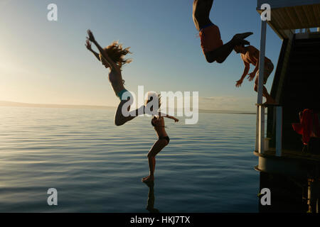 Junge Erwachsene Freunde von Sommer Hausboot in Sonnenuntergang Ozean springen Stockfoto