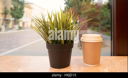 Take-away Tasse Heißgetränk und Topf mit Rasen auf Fensterbank Stockfoto