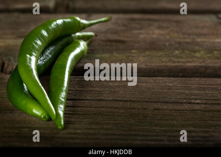 Drei grüne hot chili Peppers über alten rustikalen Holztisch mit Textfreiraum Stockfoto