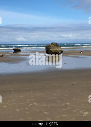 Große Felsen am Sandstrand mit blauem Himmel und Wolken. Stockfoto