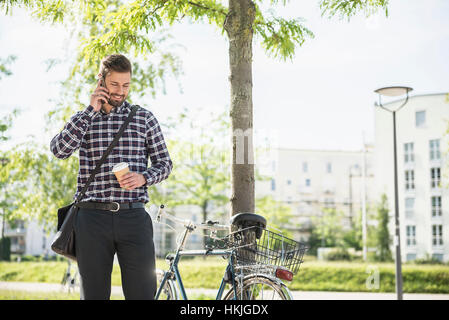 Junger Mann, telefonieren mit dem Handy und tranken Kaffee, München, Bayern, Deutschland Stockfoto