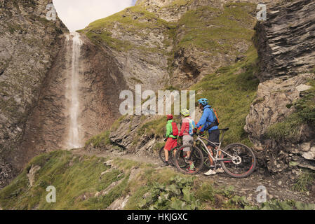 Drei Mountain-Biker-Freunde beobachten Wasserfall, Zillertal, Tirol, Österreich Stockfoto