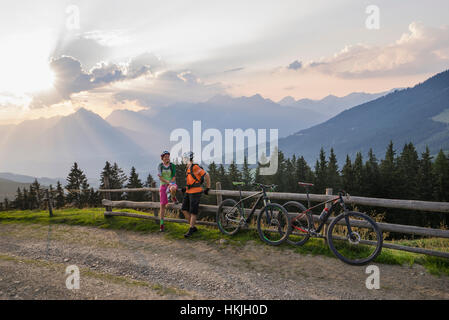 Junges Paar Mountainbiker stehen Holzzaun bei Sonnenuntergang, Zillertal, Tirol, Österreich Stockfoto