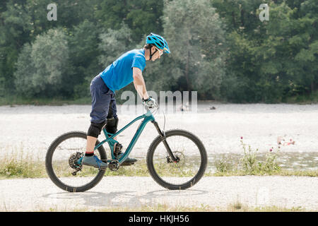 Mann reitet mit Mountainbike stehend auf Pedalen entlang Fluss, Bayern, Deutschland Stockfoto