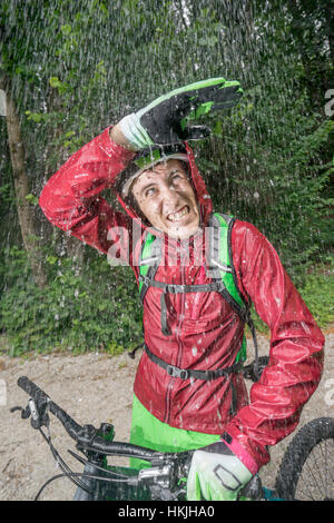 Mountainbiker stehen im Regen mit der Hand über den Kopf, Kampenwand, Bayern, Deutschland Stockfoto