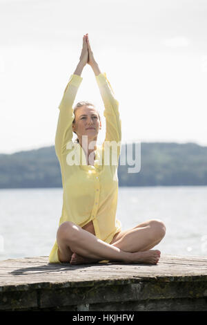 Frau beim Lotus Pose Yoga auf Steg am See, Ammersee, Oberbayern, Deutschland Stockfoto
