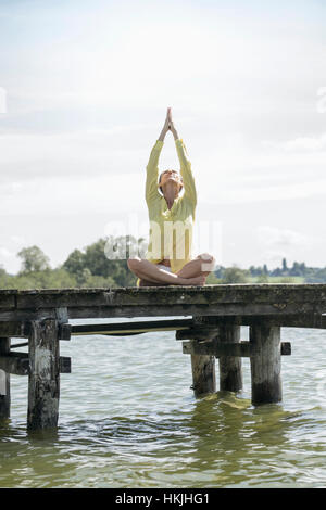 Frau beim Lotus Pose Yoga auf Steg am See, Ammersee, Oberbayern, Deutschland Stockfoto