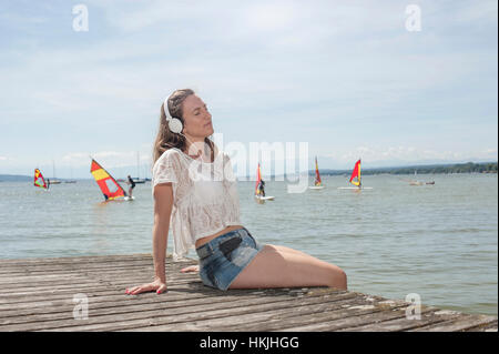 Frau, Musikhören und sitzen auf der Promenade am See, Ammersee, Oberbayern, Deutschland Stockfoto